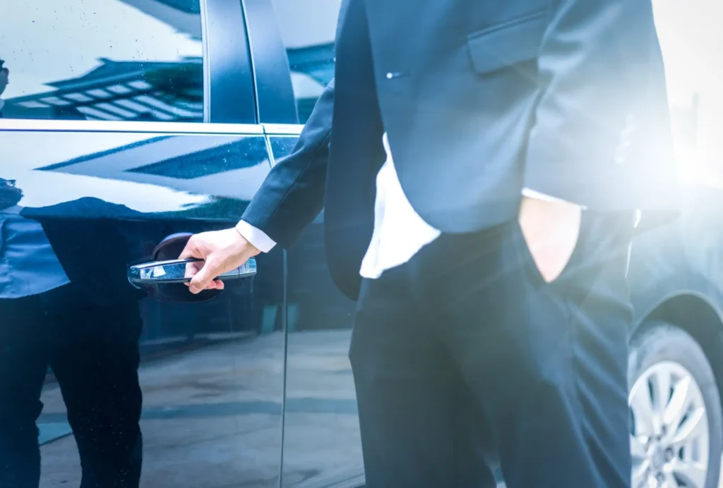 uomo con abiti eleganti apre la portiera di un'auto nera