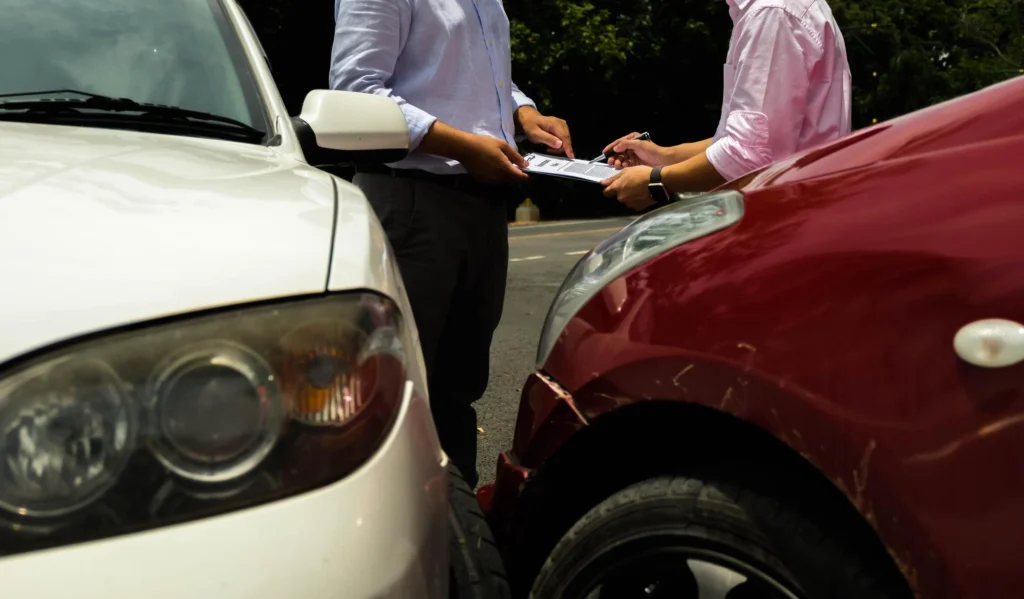 primo piano di due auto incidentate e persone che compilano la constatazione amichevole sullo sfondo