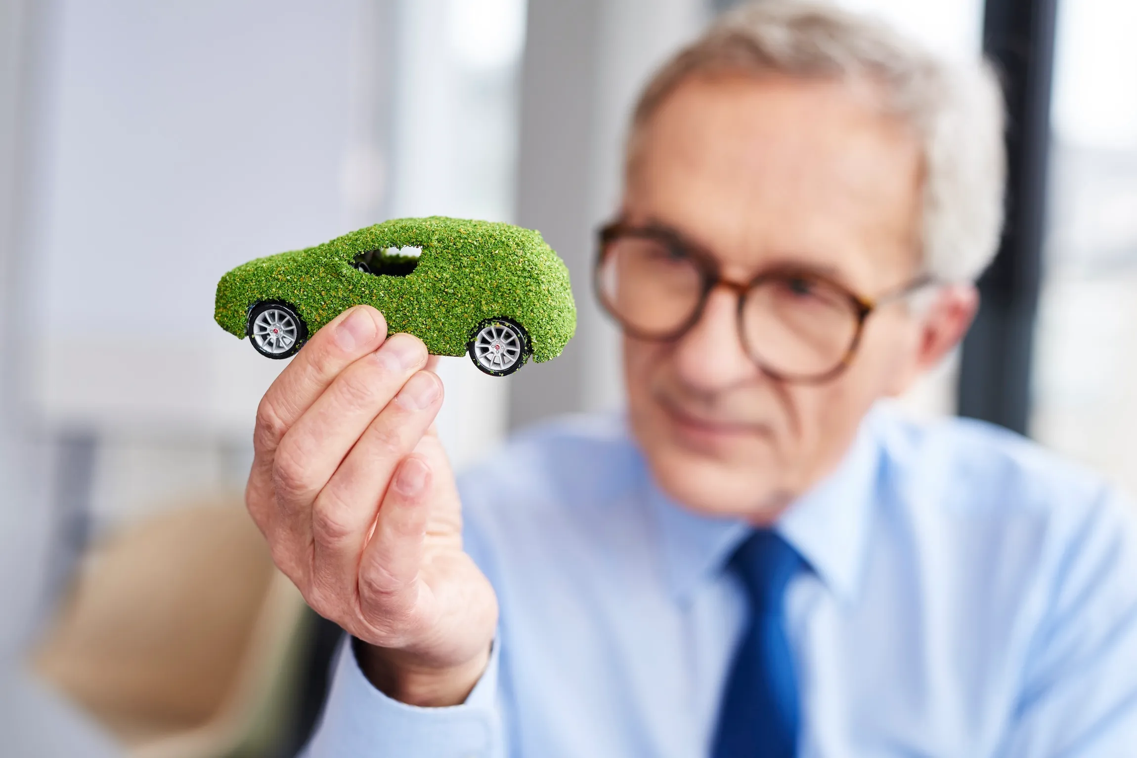 uomo che tiene in mano il modellino di un'auto fatta di erba